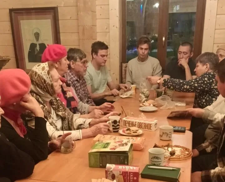 Люди сидят за столом с чаем и угощениями в светлом деревянном помещении храма