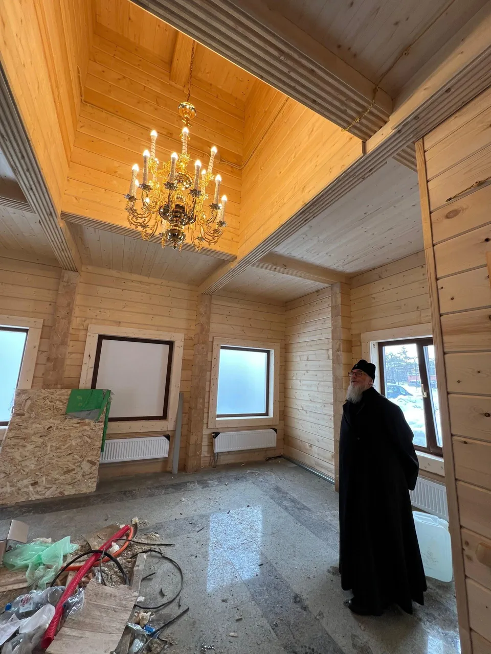 Пустое светлое помещение храма изнутри в процессе отделки, священник у окна